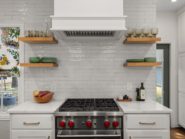 kitchen featuring light stone counters, white cabinetry, high end stove, and decorative backsplash