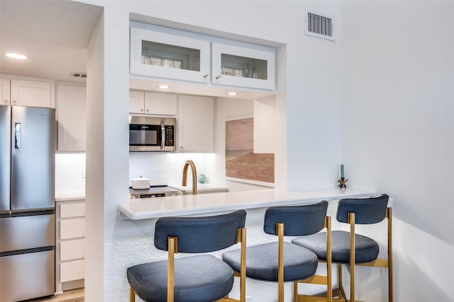 kitchen with a kitchen breakfast bar, stainless steel appliances, white cabinetry, and tasteful backsplash