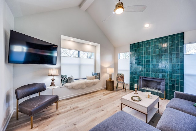 living room with ceiling fan, high vaulted ceiling, hardwood / wood-style flooring, beam ceiling, and a tiled fireplace