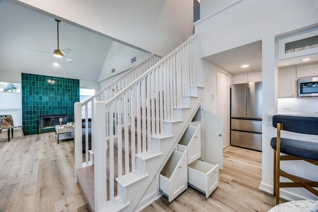 stairway with ceiling fan, wood-type flooring, vaulted ceiling, and a fireplace