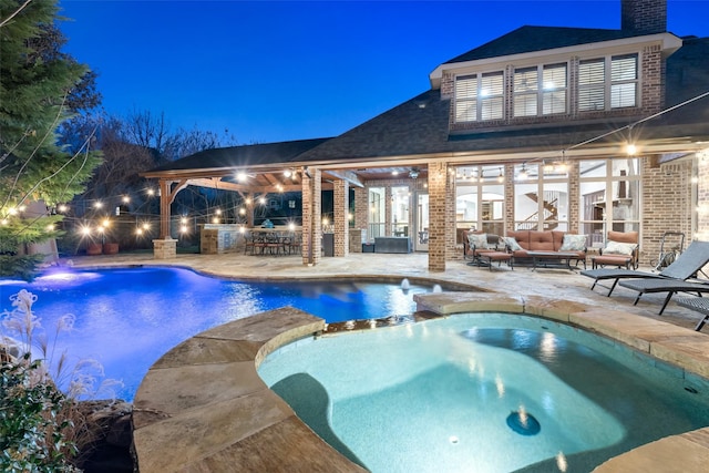 pool at twilight with an in ground hot tub, a patio, exterior bar, outdoor lounge area, and exterior kitchen