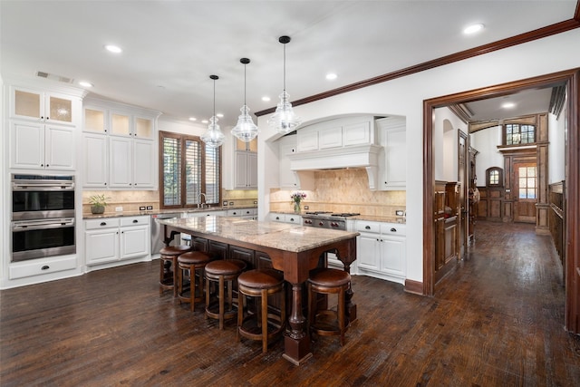 kitchen with a center island, white cabinetry, hanging light fixtures, light stone countertops, and appliances with stainless steel finishes