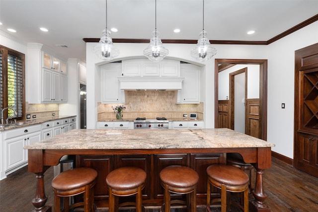 kitchen with pendant lighting, dark hardwood / wood-style flooring, light stone counters, a kitchen island, and white cabinets