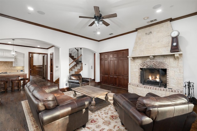 living room with a large fireplace, dark wood-type flooring, crown molding, and ceiling fan