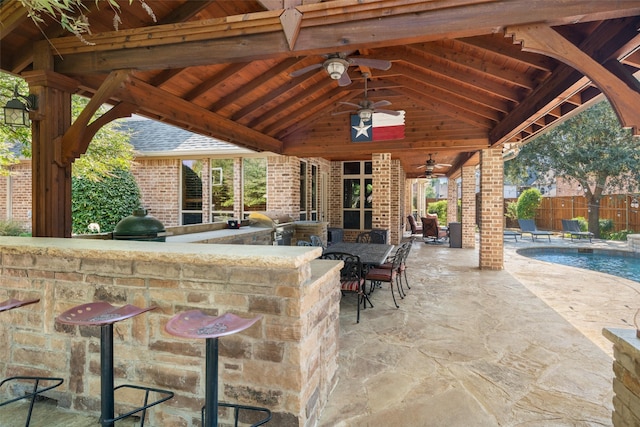 view of patio featuring grilling area, exterior kitchen, a bar, a fenced in pool, and ceiling fan