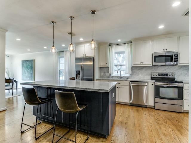 kitchen featuring appliances with stainless steel finishes, white cabinetry, decorative light fixtures, and a kitchen island