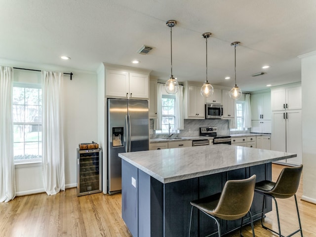 kitchen with a kitchen island, stainless steel appliances, beverage cooler, and white cabinets