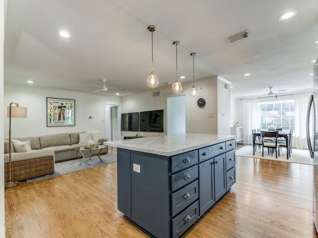 kitchen with light wood-type flooring, a center island, light stone countertops, ceiling fan, and pendant lighting