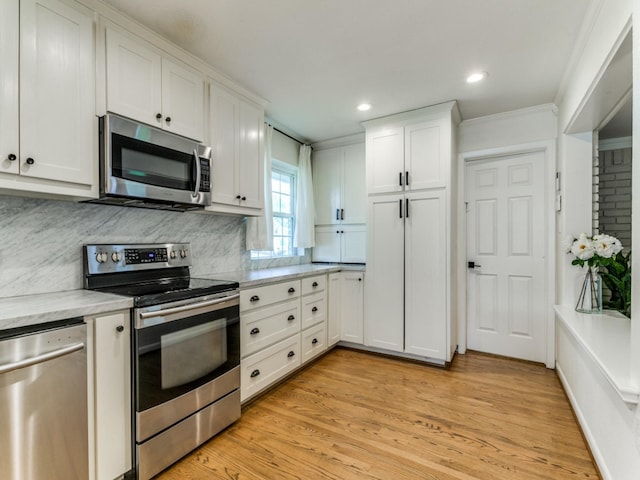 kitchen with appliances with stainless steel finishes, light wood-type flooring, crown molding, white cabinetry, and backsplash