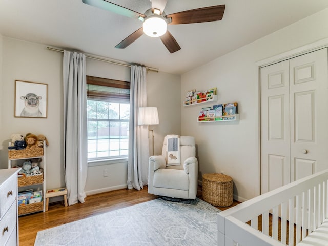 bedroom featuring a nursery area, ceiling fan, light hardwood / wood-style floors, and a closet