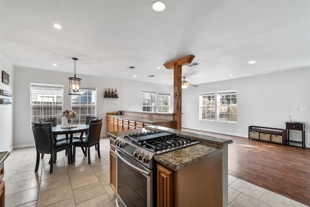 kitchen with stainless steel range with gas cooktop, decorative light fixtures, light tile patterned floors, dark stone countertops, and ceiling fan