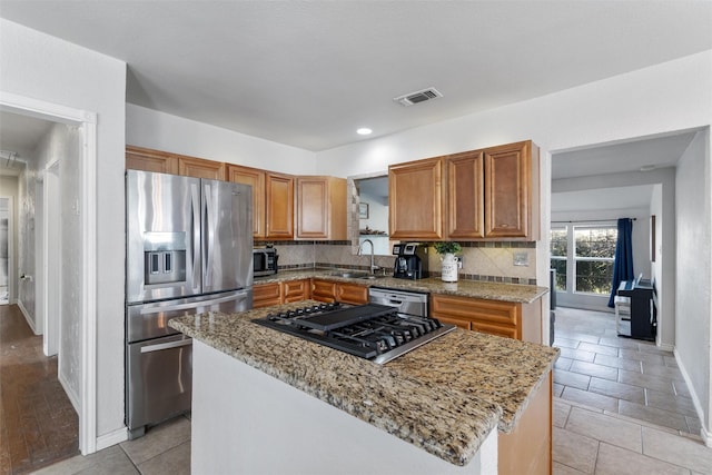 kitchen featuring a kitchen island, light stone countertops, appliances with stainless steel finishes, and tasteful backsplash