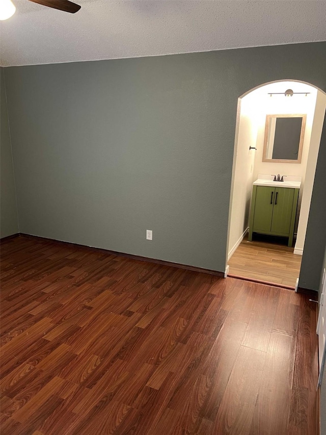 unfurnished room with sink, ceiling fan, a textured ceiling, and wood-type flooring