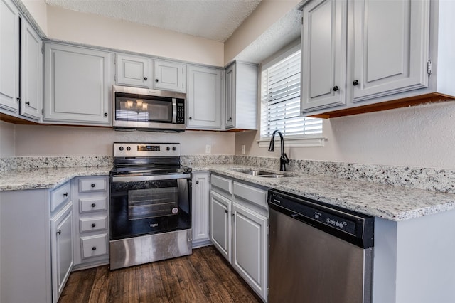 kitchen with appliances with stainless steel finishes, light stone countertops, dark hardwood / wood-style floors, a textured ceiling, and sink