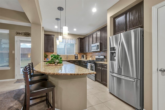 kitchen with dark brown cabinetry, decorative light fixtures, a center island, light tile patterned floors, and appliances with stainless steel finishes