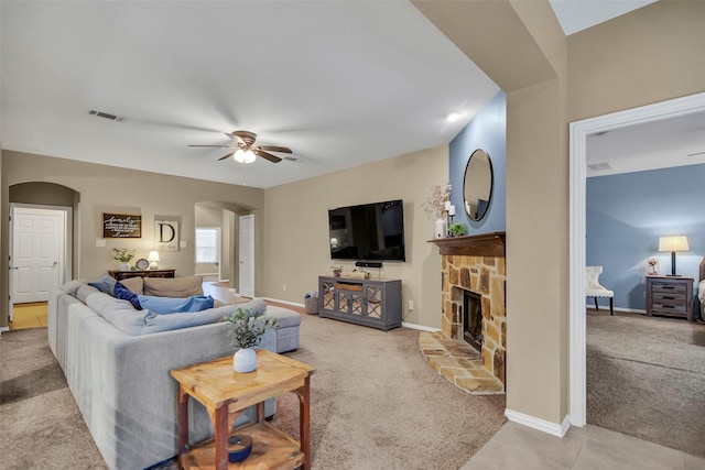 carpeted living room with ceiling fan and a stone fireplace