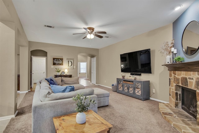 living room with ceiling fan, carpet flooring, and a stone fireplace