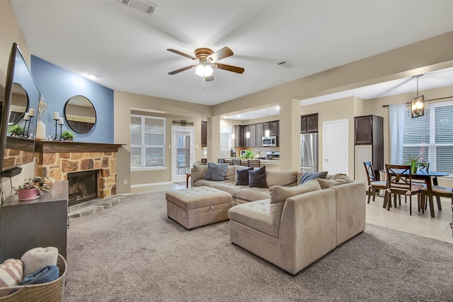 carpeted living room with a stone fireplace and ceiling fan