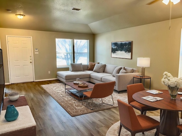 living room with wood-type flooring, a textured ceiling, ceiling fan, and vaulted ceiling