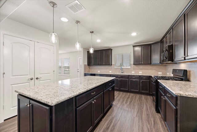 kitchen with hardwood / wood-style flooring, hanging light fixtures, black appliances, a kitchen island, and dark brown cabinets