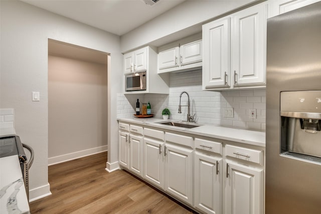 kitchen featuring white cabinets, stainless steel appliances, light wood-type flooring, sink, and backsplash