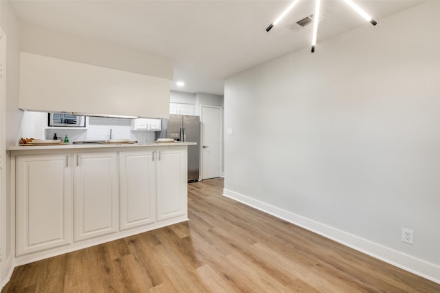 kitchen with stainless steel appliances, white cabinetry, tasteful backsplash, light hardwood / wood-style floors, and kitchen peninsula