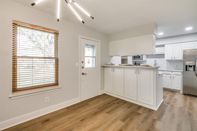 kitchen with stainless steel appliances, white cabinetry, light wood-type flooring, and backsplash