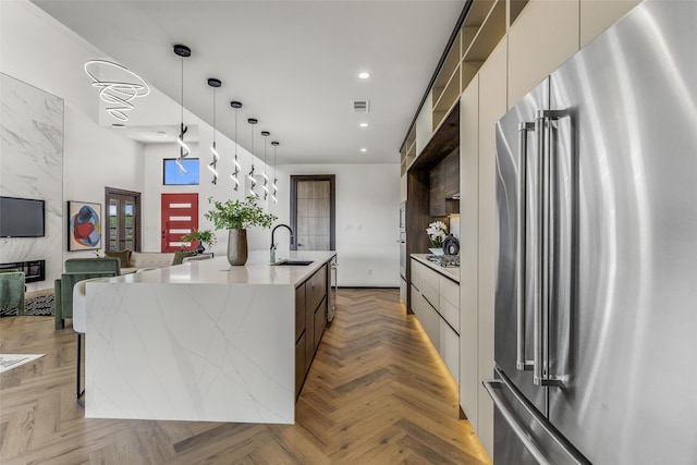 kitchen featuring pendant lighting, modern cabinets, a kitchen island with sink, high quality fridge, and light stone countertops