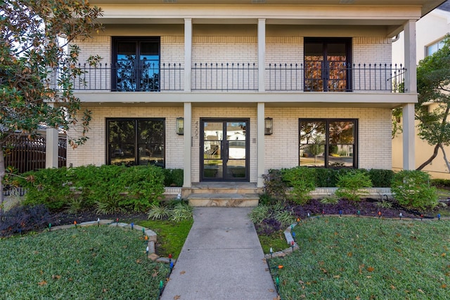 view of exterior entry featuring a lawn, french doors, and a balcony