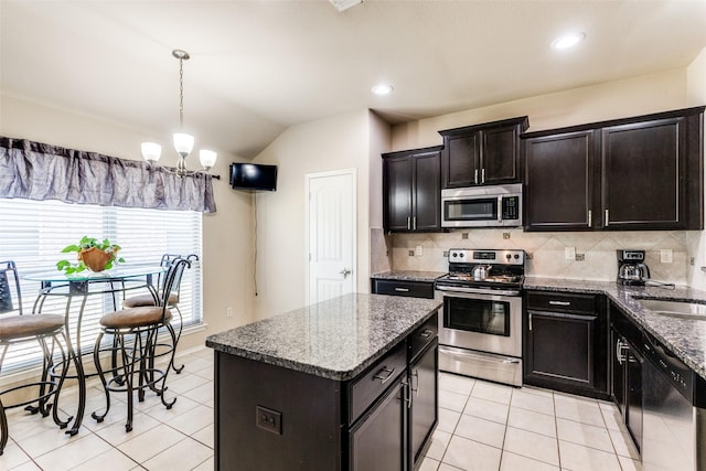 kitchen with vaulted ceiling, stainless steel appliances, a kitchen island, and dark stone counters