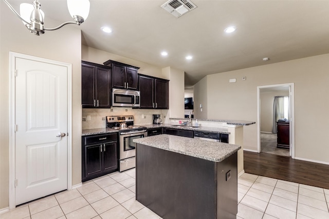 kitchen featuring appliances with stainless steel finishes, a kitchen island, hanging light fixtures, kitchen peninsula, and light tile patterned floors