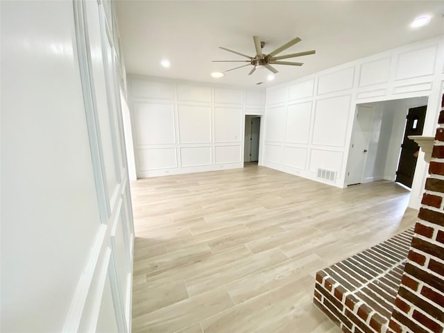 interior space with a brick fireplace, ceiling fan, and light wood-type flooring