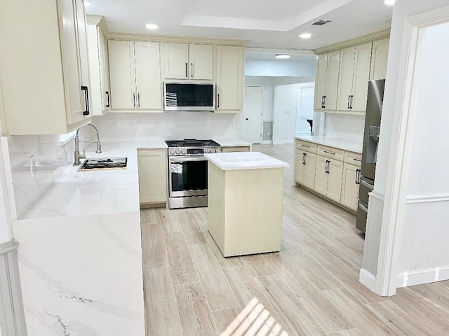 kitchen featuring stainless steel appliances, sink, a center island, cream cabinets, and light wood-type flooring