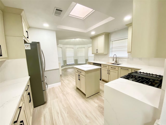 kitchen with stainless steel appliances, a kitchen island, light wood-type flooring, cream cabinetry, and sink