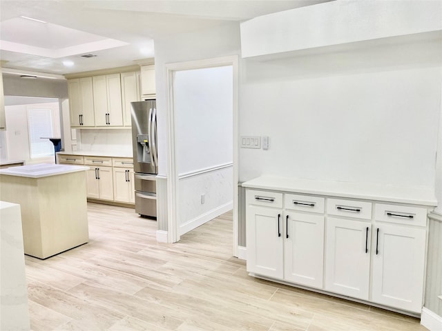 kitchen with a kitchen island, light wood-type flooring, stainless steel fridge with ice dispenser, and a tray ceiling