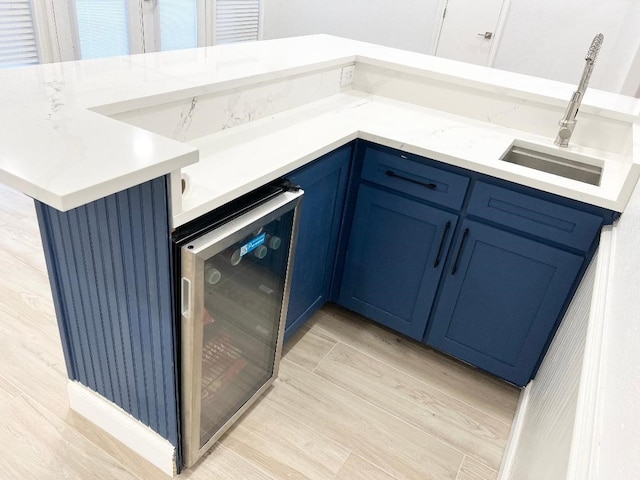 kitchen with beverage cooler, kitchen peninsula, light stone countertops, sink, and blue cabinets