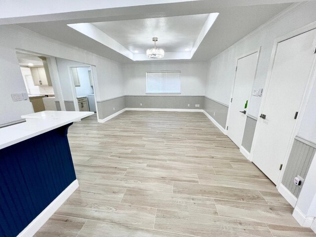 unfurnished dining area featuring a raised ceiling, an inviting chandelier, light hardwood / wood-style floors, and crown molding