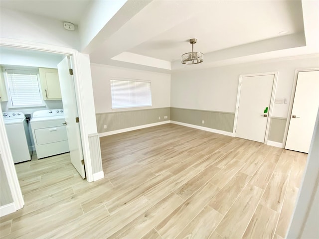 spare room featuring a raised ceiling, separate washer and dryer, light hardwood / wood-style flooring, and an inviting chandelier