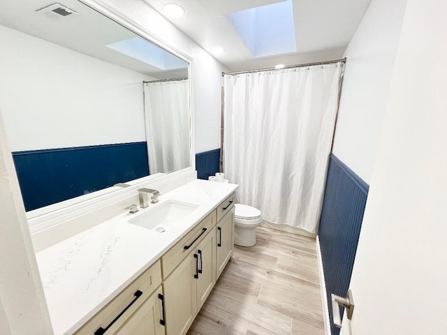 bathroom with hardwood / wood-style floors, toilet, a skylight, and vanity