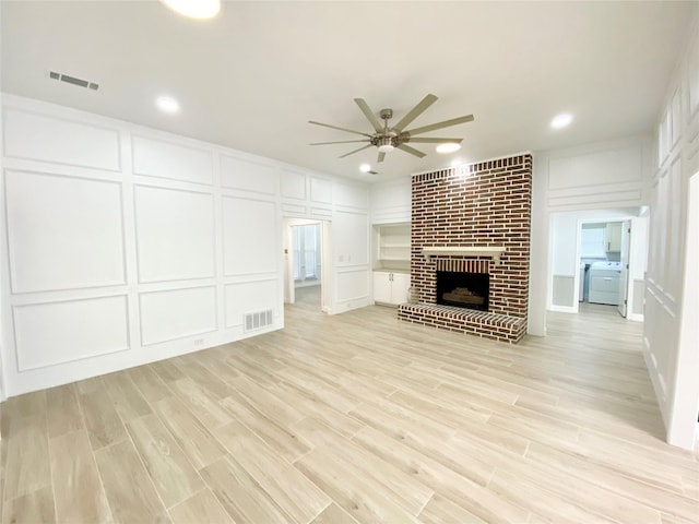 unfurnished living room featuring light wood-type flooring, a fireplace, washer / clothes dryer, and ceiling fan