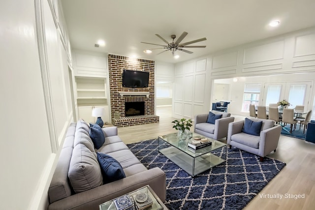 living room featuring ceiling fan, a brick fireplace, built in shelves, and hardwood / wood-style flooring