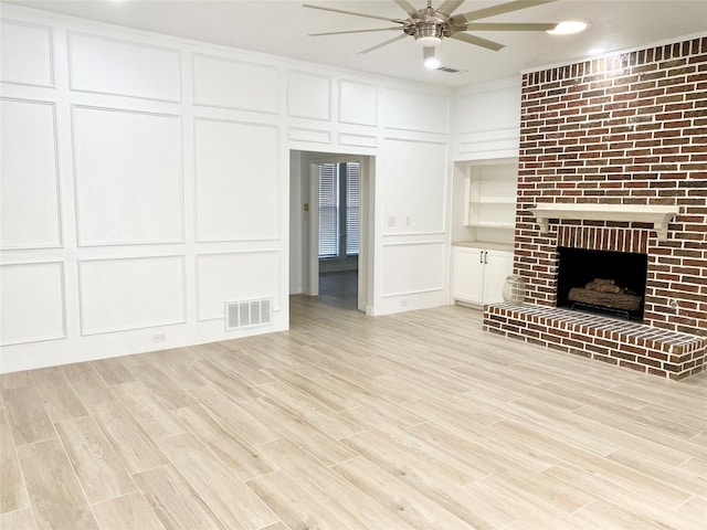 unfurnished living room with a fireplace, ceiling fan, light hardwood / wood-style floors, and built in features