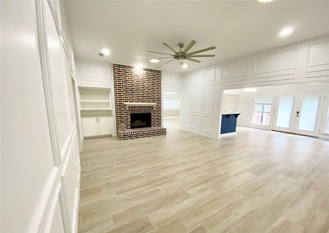 unfurnished living room featuring light hardwood / wood-style flooring, french doors, a fireplace, built in features, and ceiling fan