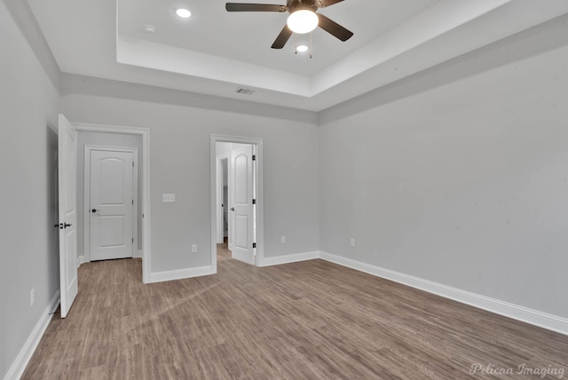 unfurnished bedroom featuring a raised ceiling, ceiling fan, and light wood-type flooring