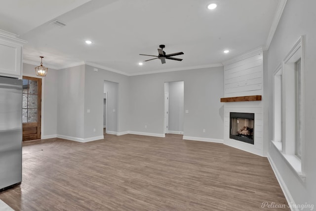 unfurnished living room featuring ceiling fan with notable chandelier, light wood-type flooring, crown molding, and a fireplace