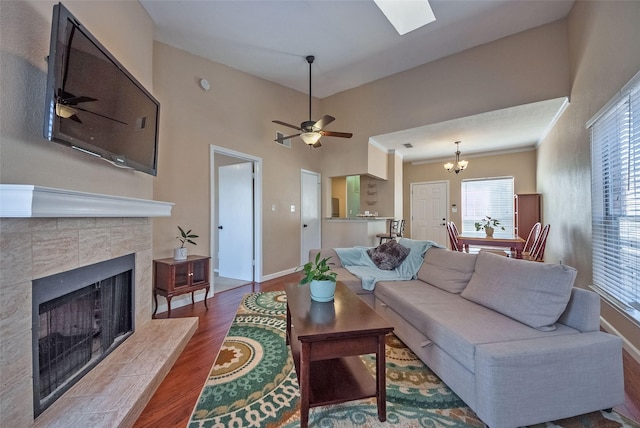 living room with ceiling fan with notable chandelier, hardwood / wood-style flooring, crown molding, and a fireplace