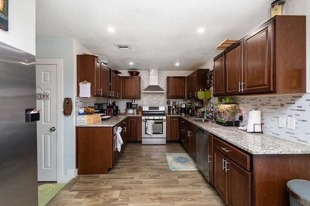 kitchen with sink, light wood-type flooring, stainless steel appliances, light stone countertops, and wall chimney range hood