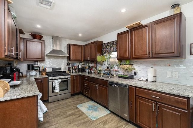 kitchen featuring sink, appliances with stainless steel finishes, light stone countertops, light hardwood / wood-style floors, and wall chimney range hood