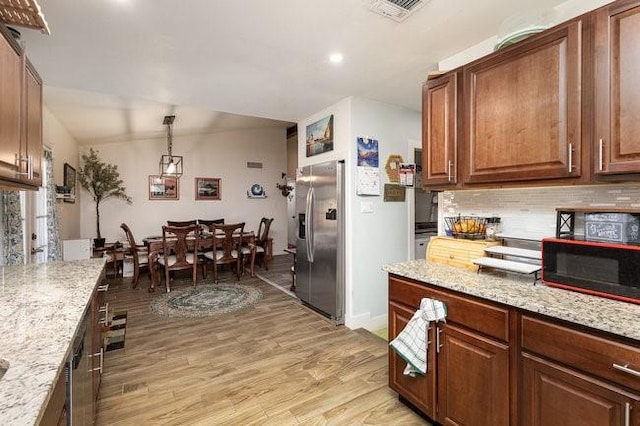 kitchen with tasteful backsplash, stainless steel refrigerator with ice dispenser, light stone counters, and light hardwood / wood-style floors