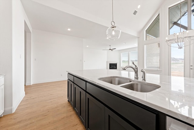 kitchen with light stone counters, sink, light hardwood / wood-style flooring, decorative light fixtures, and ceiling fan with notable chandelier